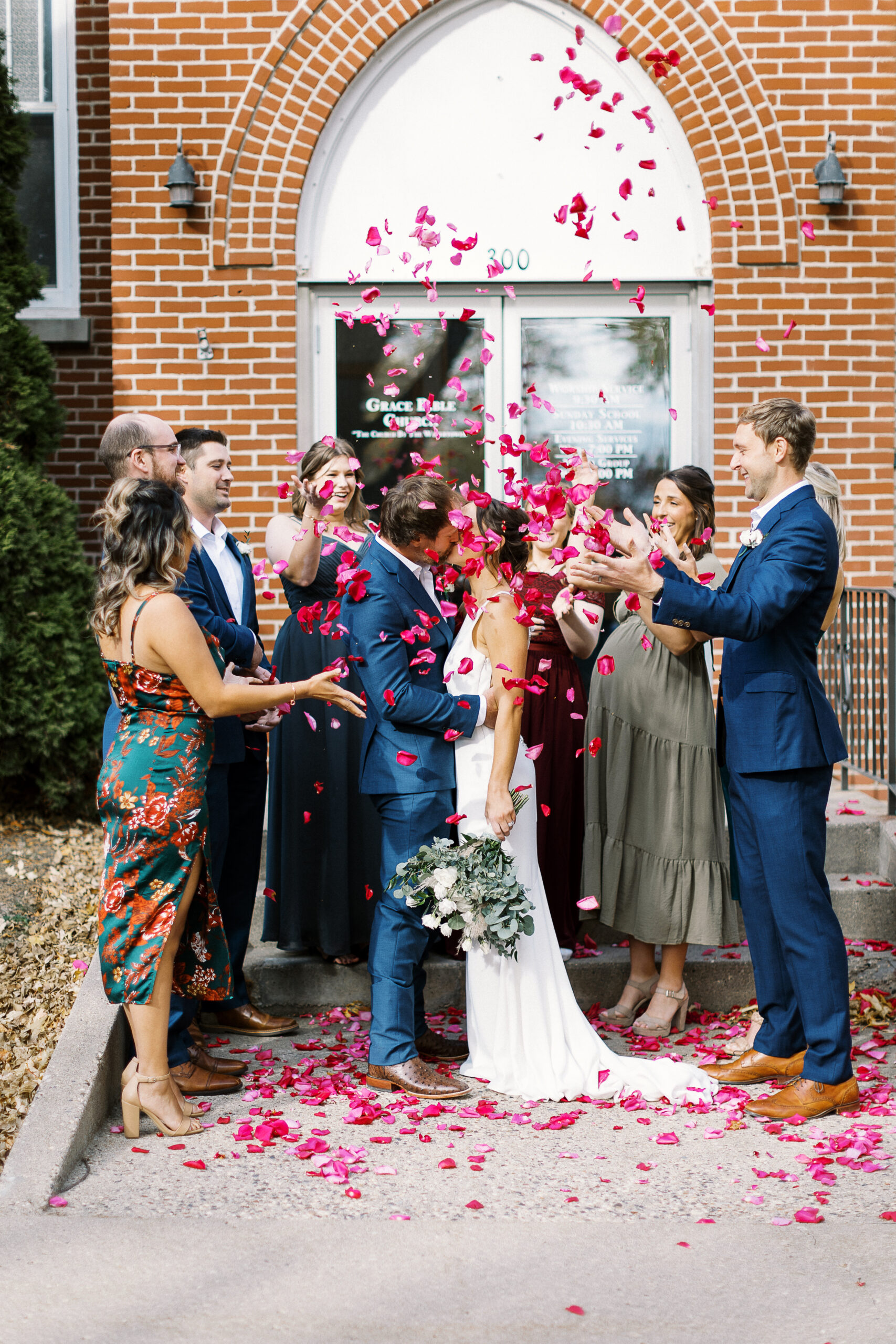 Bride and groom surrounded by guests tossing rose petals, celebrating joyfully as they exit the wedding ceremony.