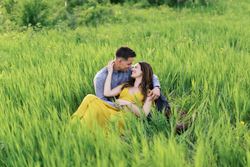 Woman lies on her partner’s lap in tall grass as he gazes into her eyes; she smiles and gently touches his hair.