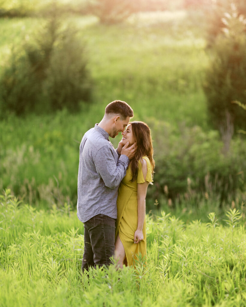He leans in close to kiss her as she smiles, holding her dress in tall green grass, captured by Minnesota wedding photographer Toly Dzyuba.