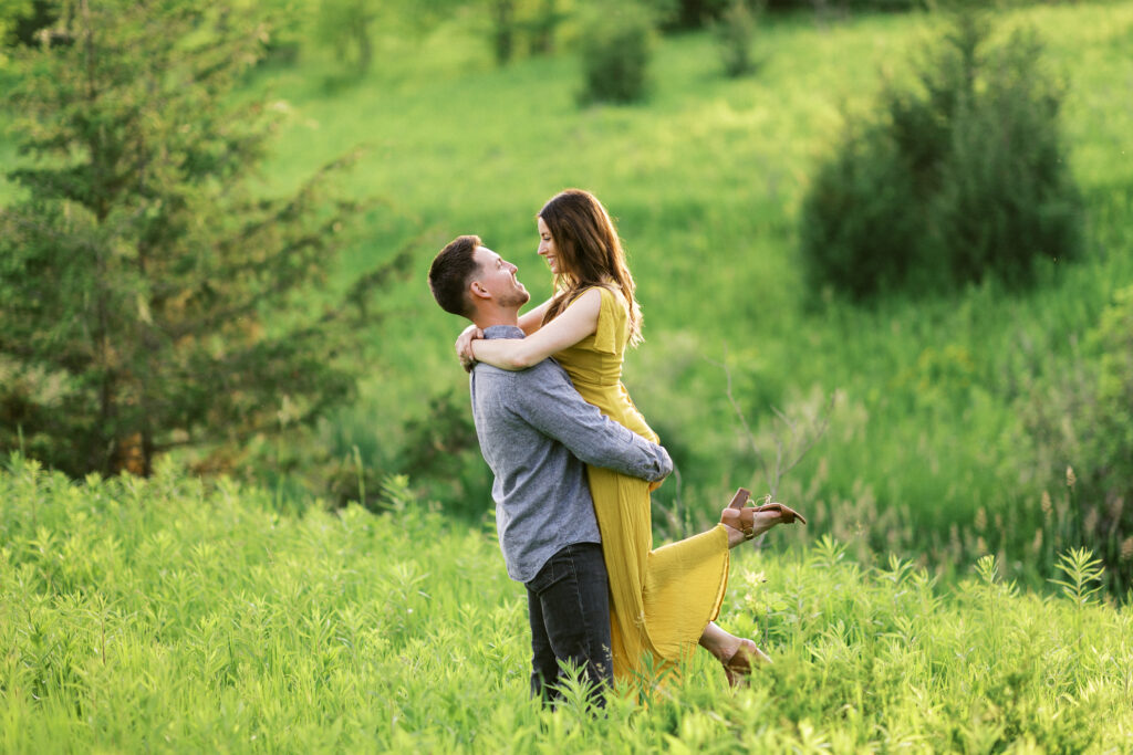 Groom lifts his bride into the golden sunset amid the tall grass at Elm Creek Park Reserve in Maple Grove and about to kiss her as she wraps her arms around his neck. Captured by Minnesota wedding photographer Toly Dzyuba.