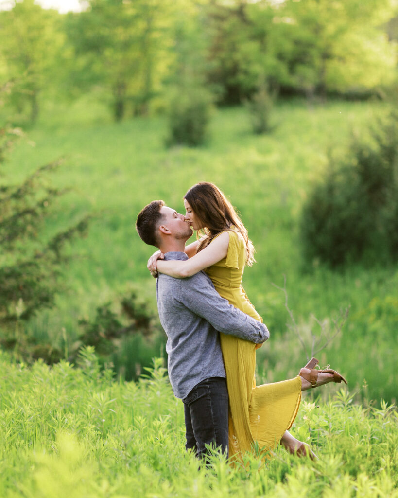 Groom lifts his bride into the golden sunset amid the tall grass at Elm Creek Park Reserve in Maple Grove and kisses her as she wraps her arms around his neck. Captured by Minnesota wedding photographer Toly Dzyuba.