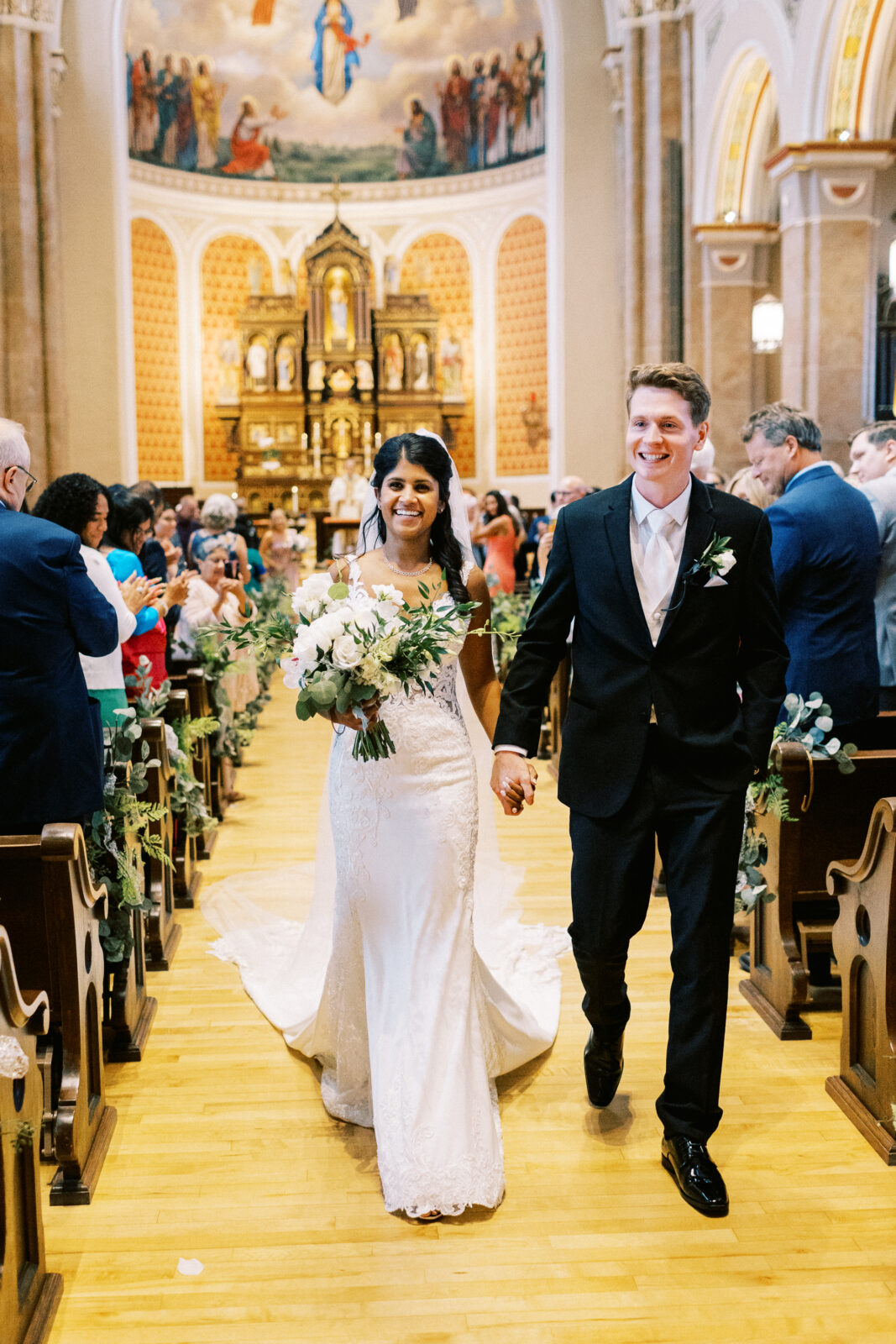 Bride and groom walk out of the Church as husband and wife, celebrating their marriage while guests cheer with joy. Their faces are lit with joyful smiles and emotion.