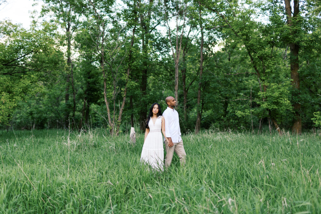A couple stands in nature, holding hands and looking in opposite directions, surrounded by tall grass at Elm Creek Park.