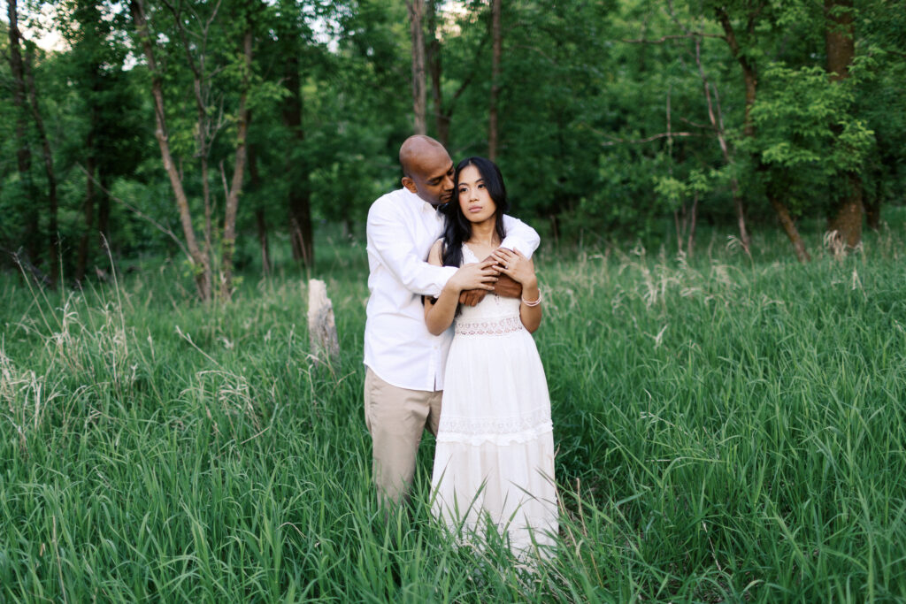The couple embraces each other, standing together in the serene natural beauty of Elm Creek Park.