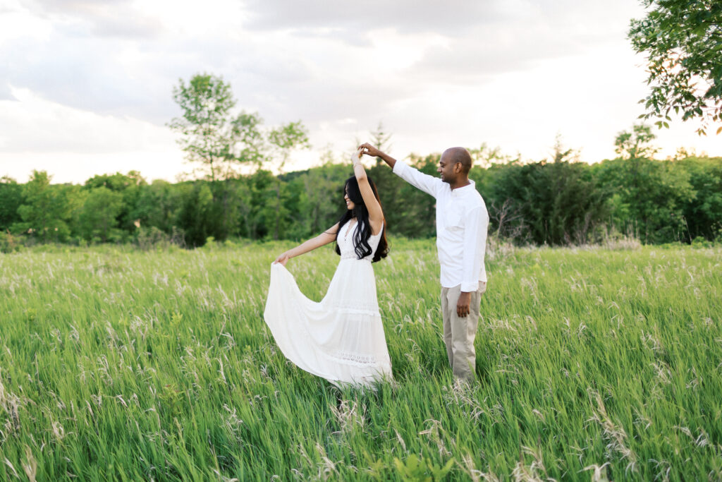 He gently holds her hand as she twirls in the golden sunset at Elm Creek Park, creating a magical and romantic moment.