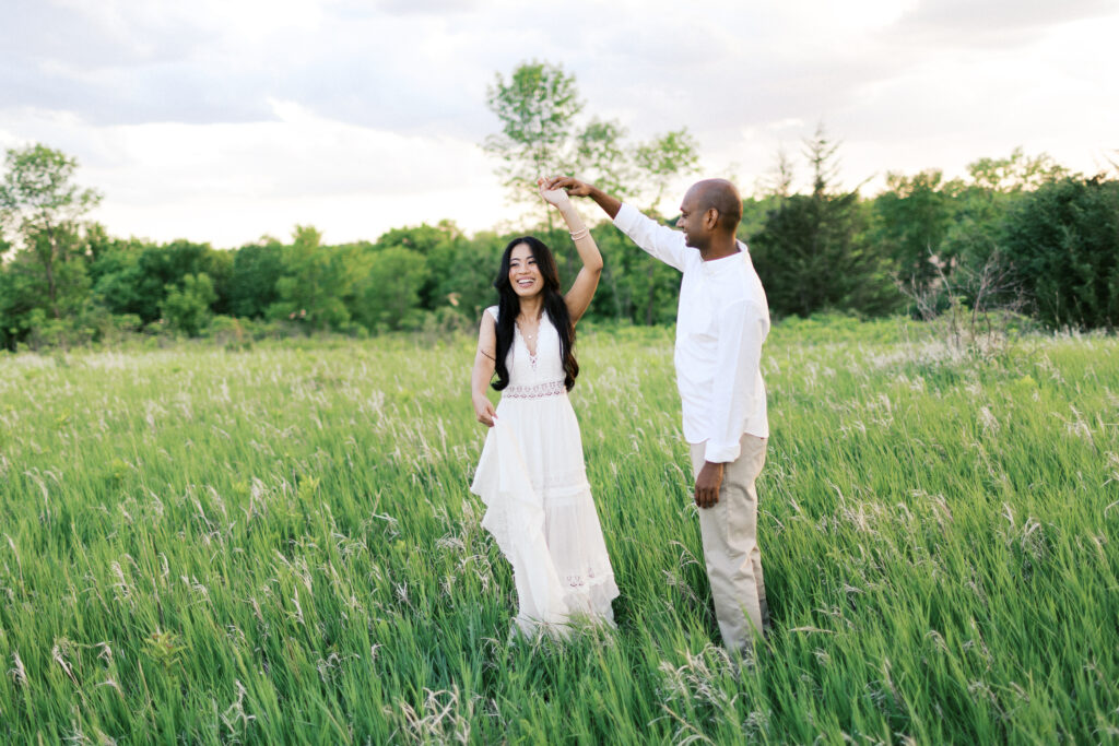 He holds her hand as she twirls with a smile at Elm Creek Park Reserve in Maple Grove, captured by Minnesota wedding photographer Toly Dzyuba.
