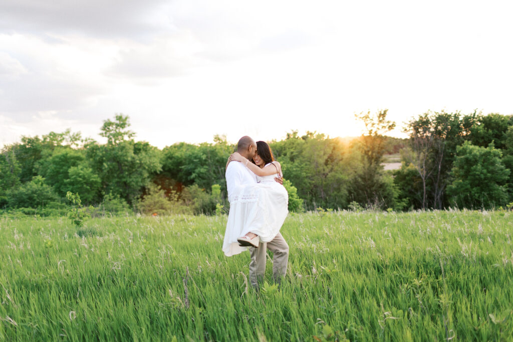 He lifts her in his arms and spins her slowly, holding her close to his heart as they look into each other’s eyes smiling, bathed in the golden sunset at Elm Creek Park in Maple Grove. Captured by Minnesota wedding photographer Toly Dzyuba.