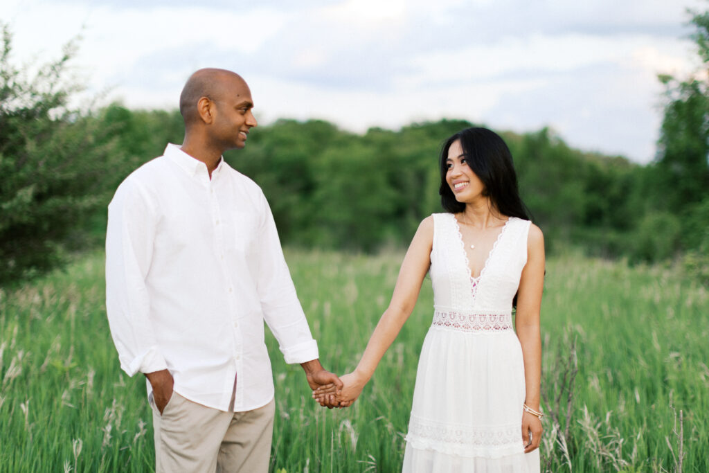Maple Grove Engagement session. Couple holding hands, looking into each other’s eyes, and smiling warmly, capturing a moment of deep connection and love.