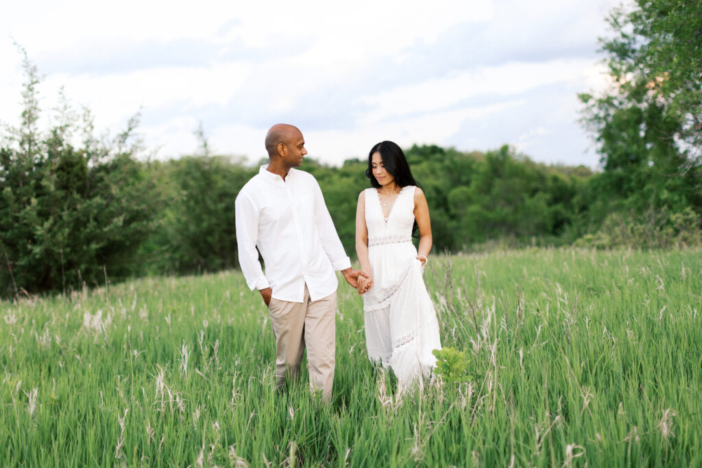 Maple Grove Engagement session. Dominic holds Wendy's hand as they stroll through the tall grass at Elm Creek Park Reserve in Maple Grove, both smiling joyfully.