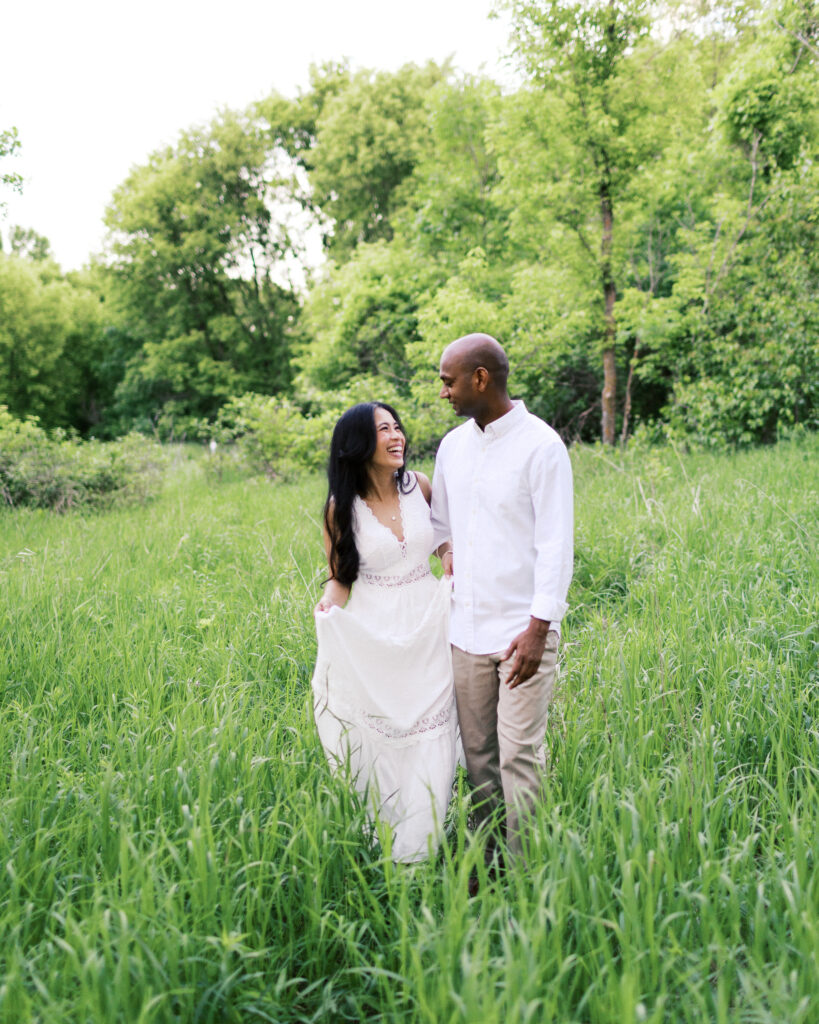 The couple holds hands, walking together through tall grass, laughing and enjoying a romantic moment at Elm Creek Park Reserve.