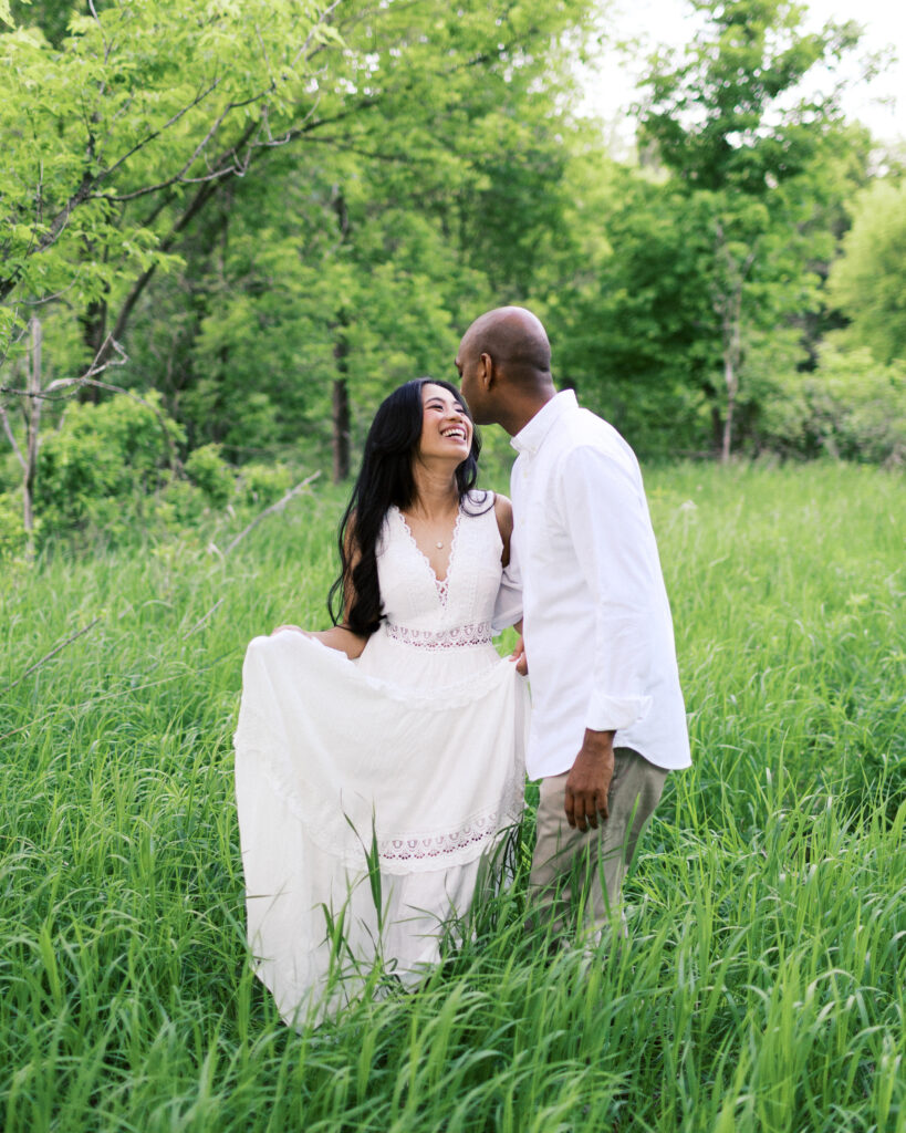 They walk together, strolling closely through the grass, laughing and enjoying each other’s company in a joyful moment.