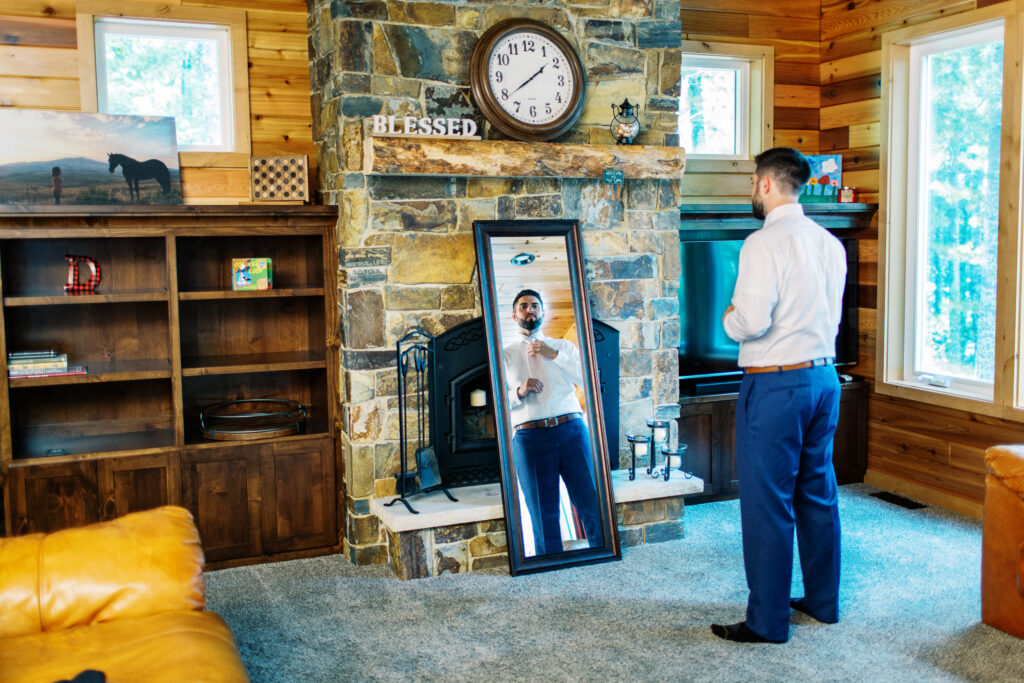 Groom getting ready at the cabin in Webster Wisconsin. He is standing by the mirror adjusting his tie for his wedding day.