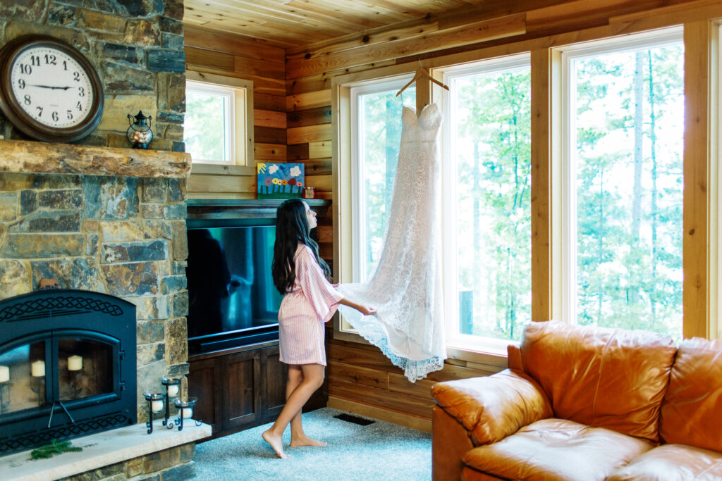 Bride looking at her wedding dress hanging on the huge window at the cabin in Webster, WI.