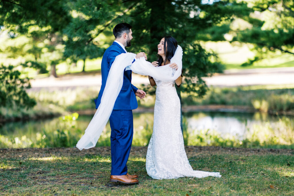 First look under a tree at Elopment for the bride and groom in Webster, Wisconsin. The bride and groom are standing under a tree. The bride has a long veil that is flowing in the air and she is laughing and tears of joy are flowing down her face. She is really excited to see the groom.