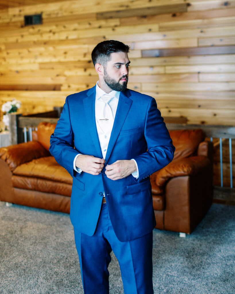 Groom buttoning his navy jacket.