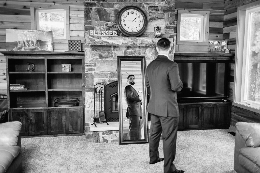 Groom looking in the mirror and buttoning his wedding suit.