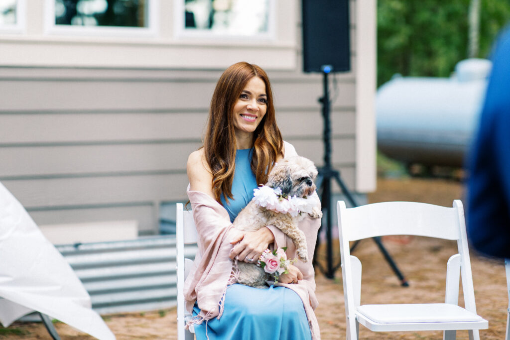 Mom sits on a chair with a pup at her daughter's elopement with a smile. A true heartfelt Cabin Elopement in Webster, WI | Minnesota Wedding Photographer.