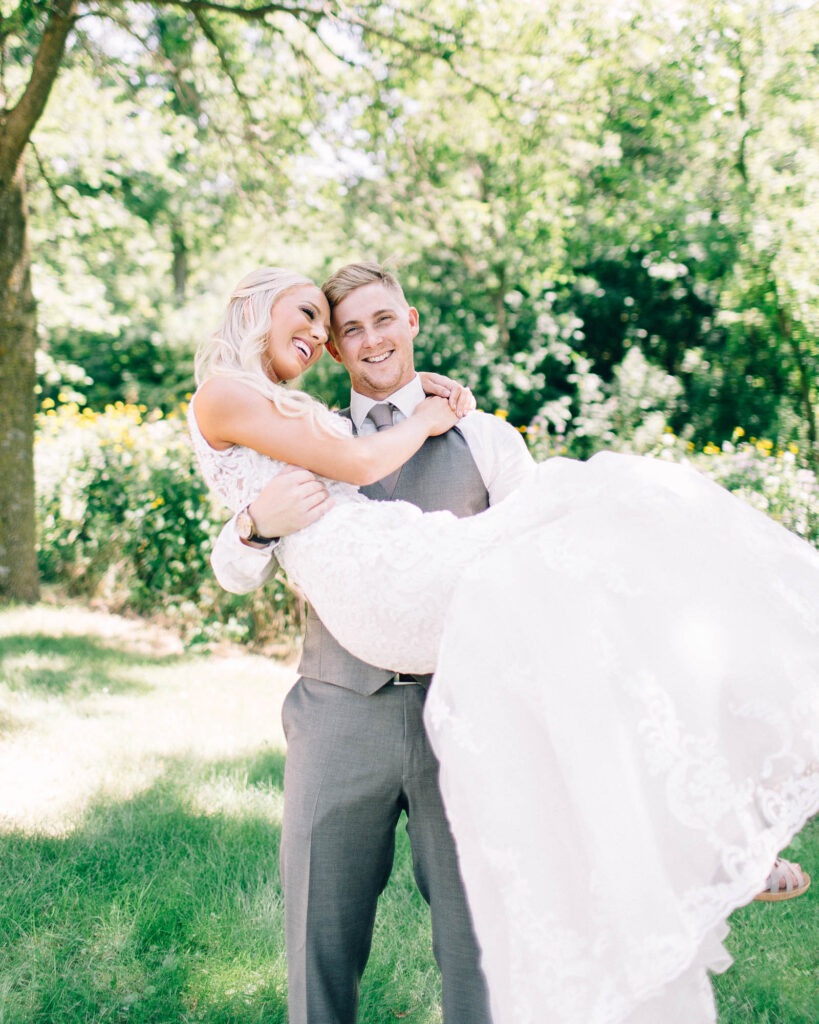 Groom lifts his bride into his arms as they share a joyful, smiling moment together.