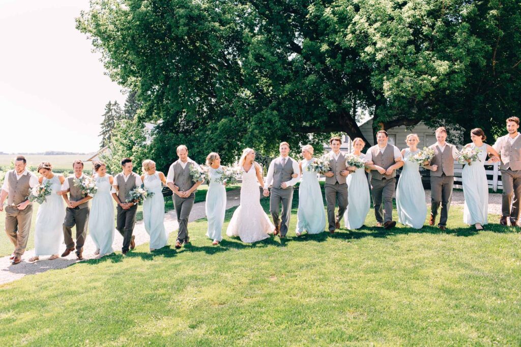 A large wedding group walking together with linked arms, smiling and laughing with joy at Legacy Hill Farm.