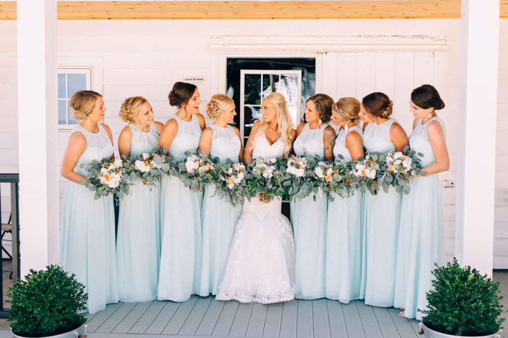 Bride squad sharing joyful smiles, dressed in gorgeous teal gowns and holding their beautiful bouquets at Legacy Hill Farm.