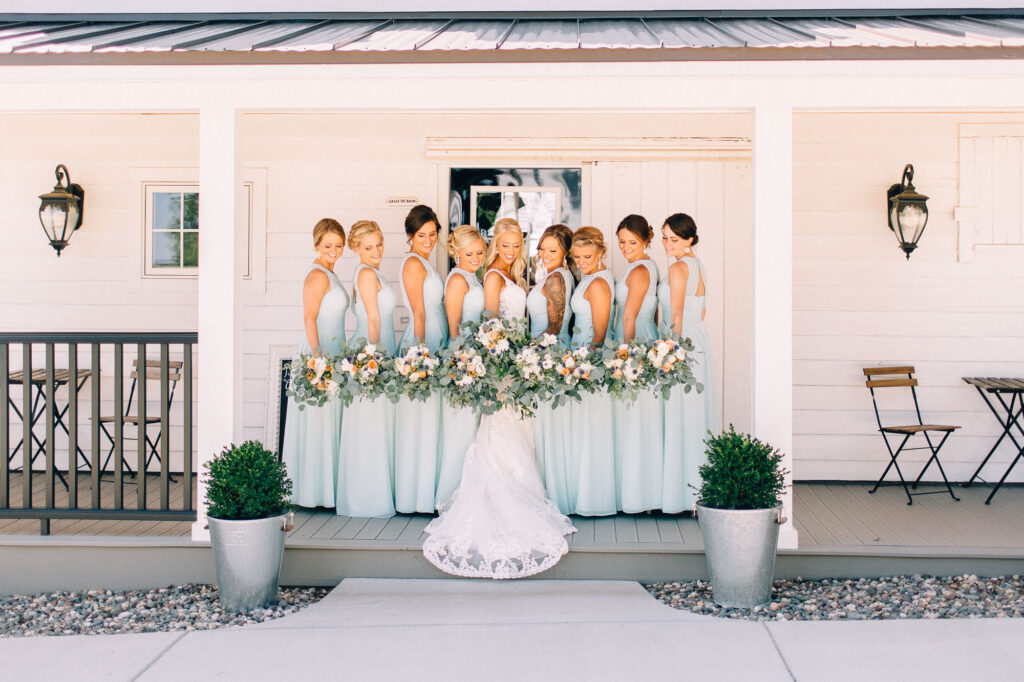 Bridesmaids standing together on the porch, admiring their gorgeous flowers at Legacy Hill Farm, captured by Minnesota wedding photographer.