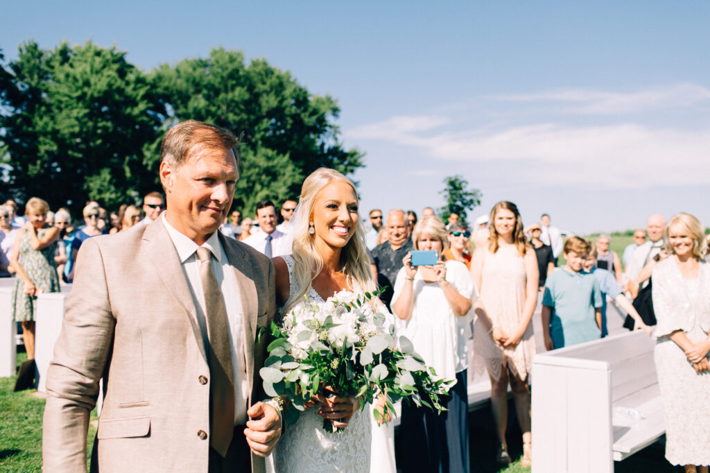 Bride and her dad walking down the aisle, both smiling, during the wedding ceremony at Legacy Hill Farm.