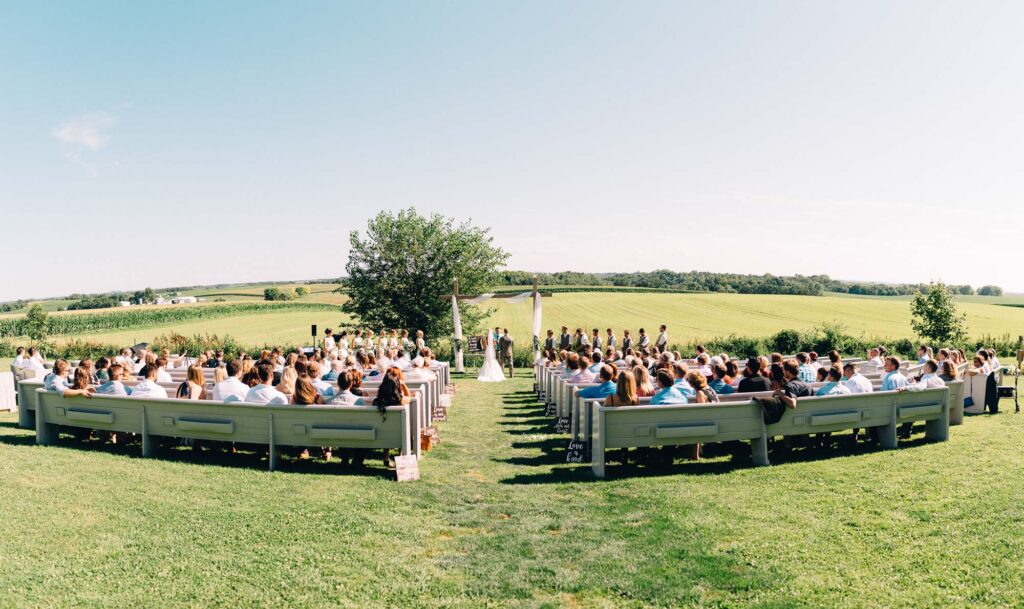 Wedding party standing during the ceremony, overlooking the beautiful farmland and peaceful sky, with guests seated at Legacy Hill Farm.