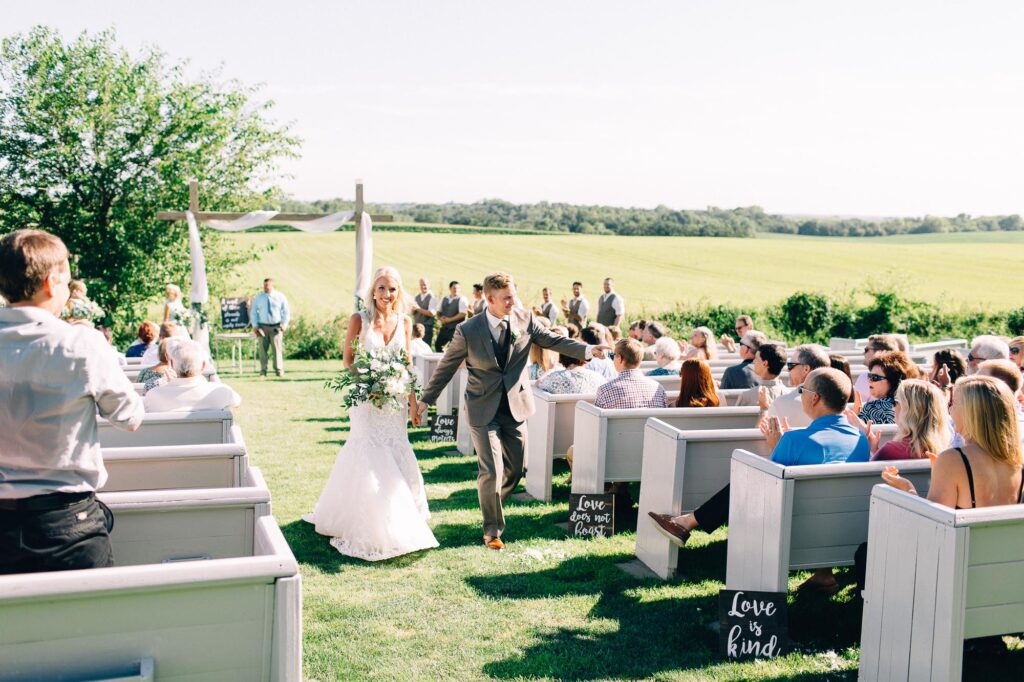 Bride and groom walking out of the ceremony holding hands, smiling with joy as the groom fist bumps a guest at Legacy Hill Farm, captured by Toly Dzyuba Photography.
