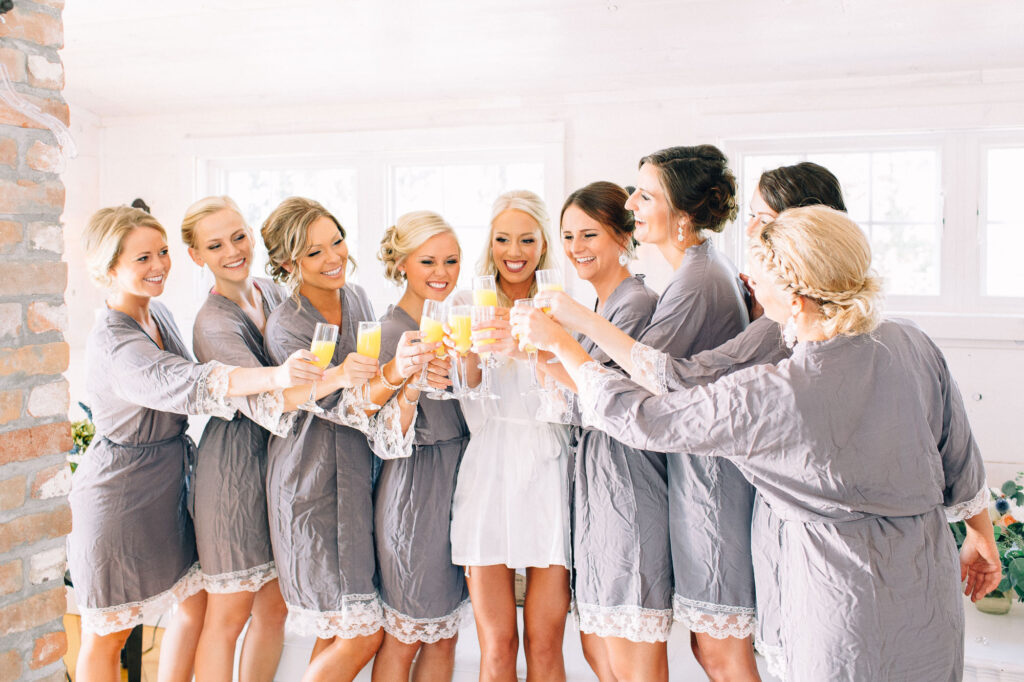 Bride squad toasting with drinks in their robes before getting dressed, celebrating with the bride at Legacy Hill Farm.