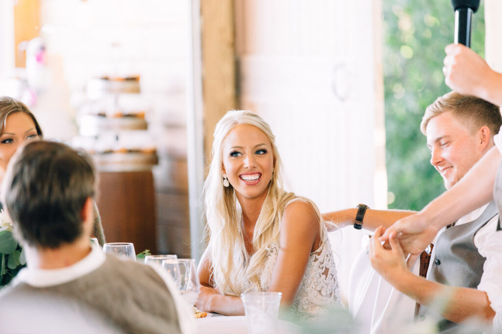 Bride sitting at her wedding and listening to the speech smiling.