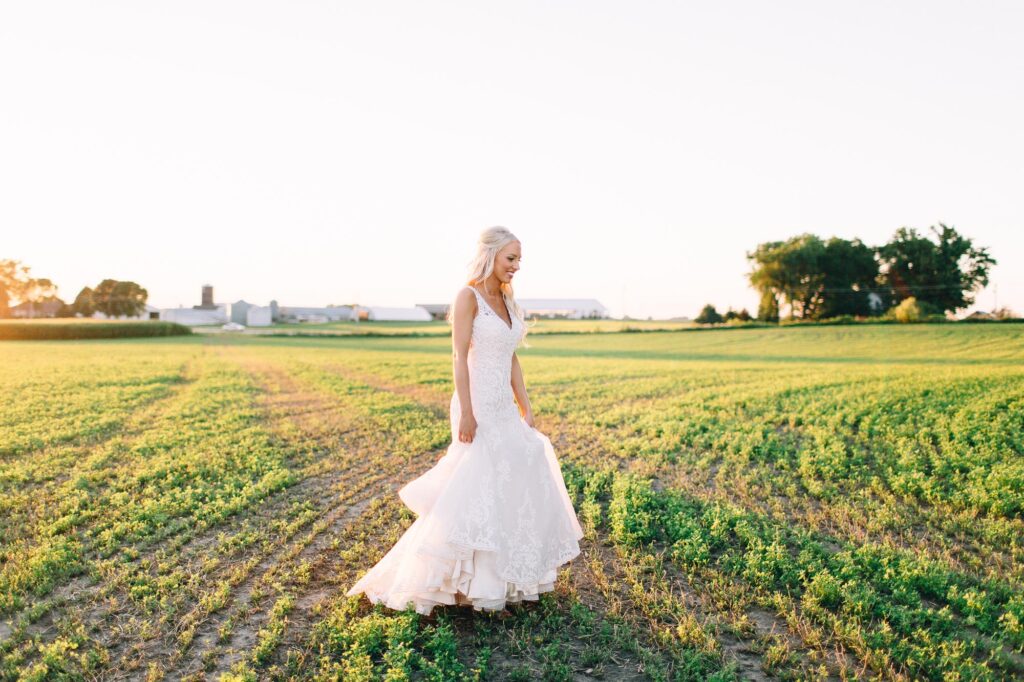 Bride holding her dress with her hands, walking across the field with the sunset glowing in the background at Legacy Hill Farm.
