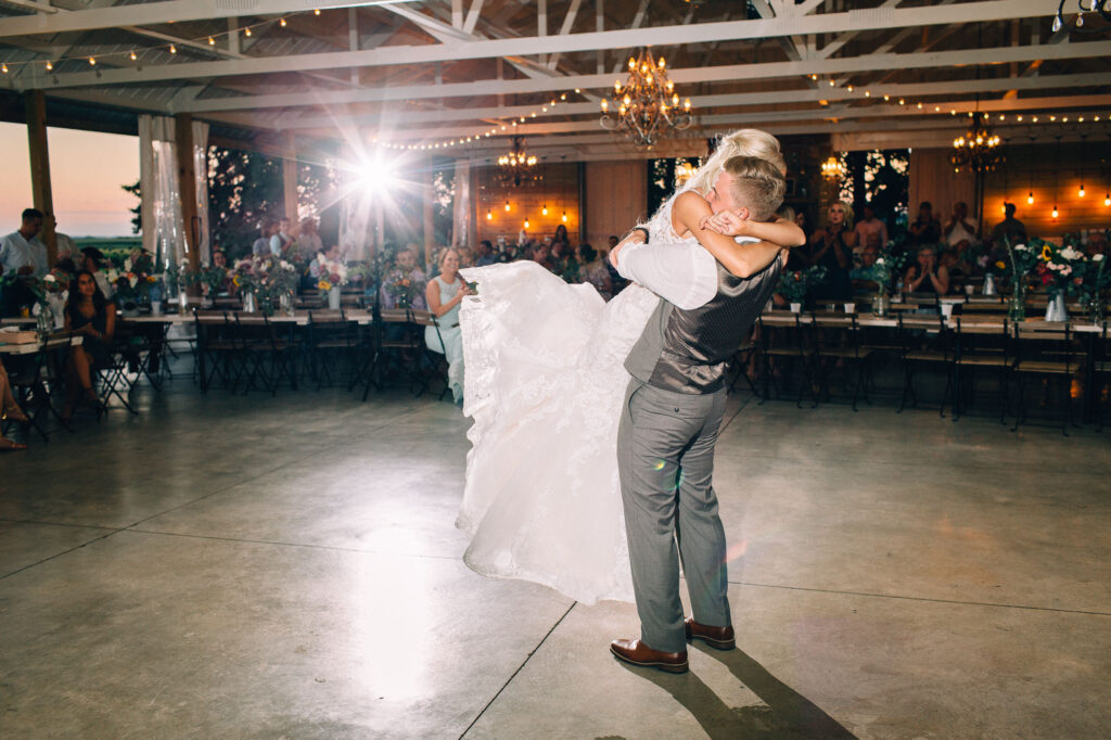 Groom lifts the bride off the ground, with her feet in the air, during their first dance at dawn at Legacy Hill Farm.