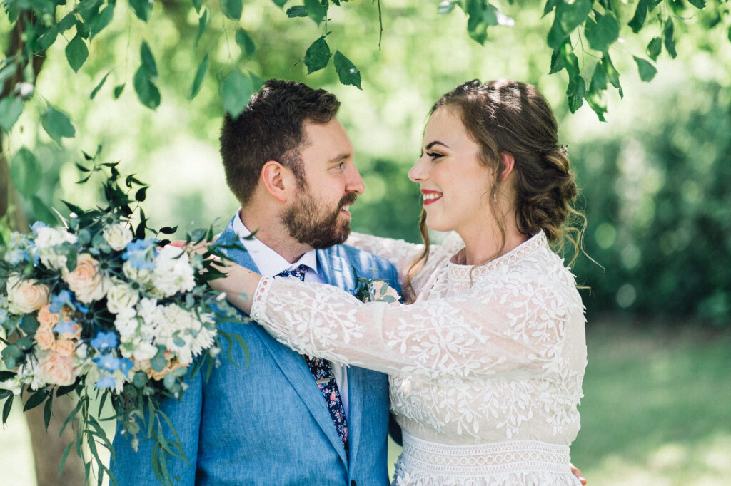 Bride with her arm draped over her groom's shoulder, holding a bouquet while gazing into his eyes with a loving smile. Captured by Minneapolis wedding photographer.