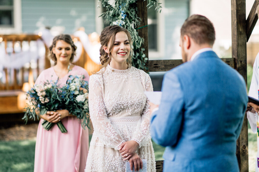 Bride stand with her arms crossed and smiles at her wedding ceremony at their summer backyard wedding in Minneapolis.