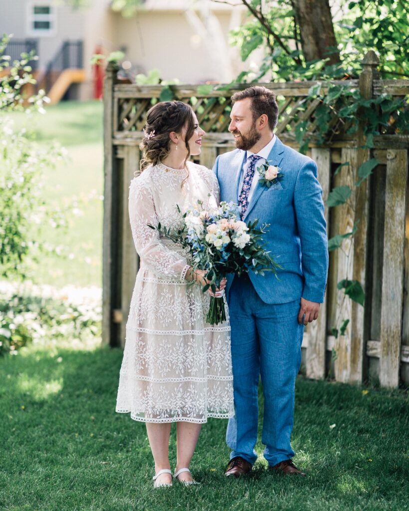 Bride and groom standing next to each other looking at each other with big smiles at the summer backyard wedding in Minneapolis.