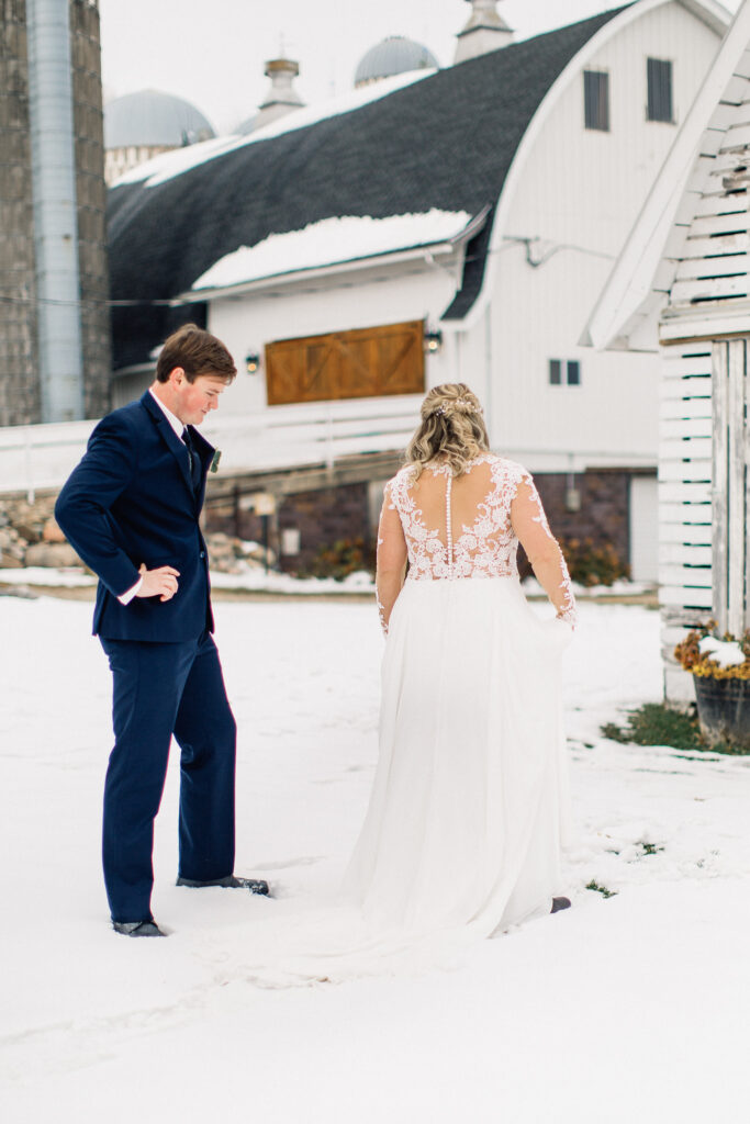 Groom looking at the bride beautiful wedding gown on the snowy ground.