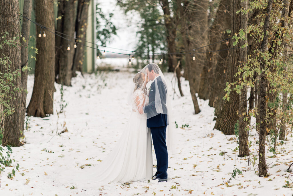 Bride and groom kissing under the vail on wintry day at The Cottage Farmhouse winter wedding.