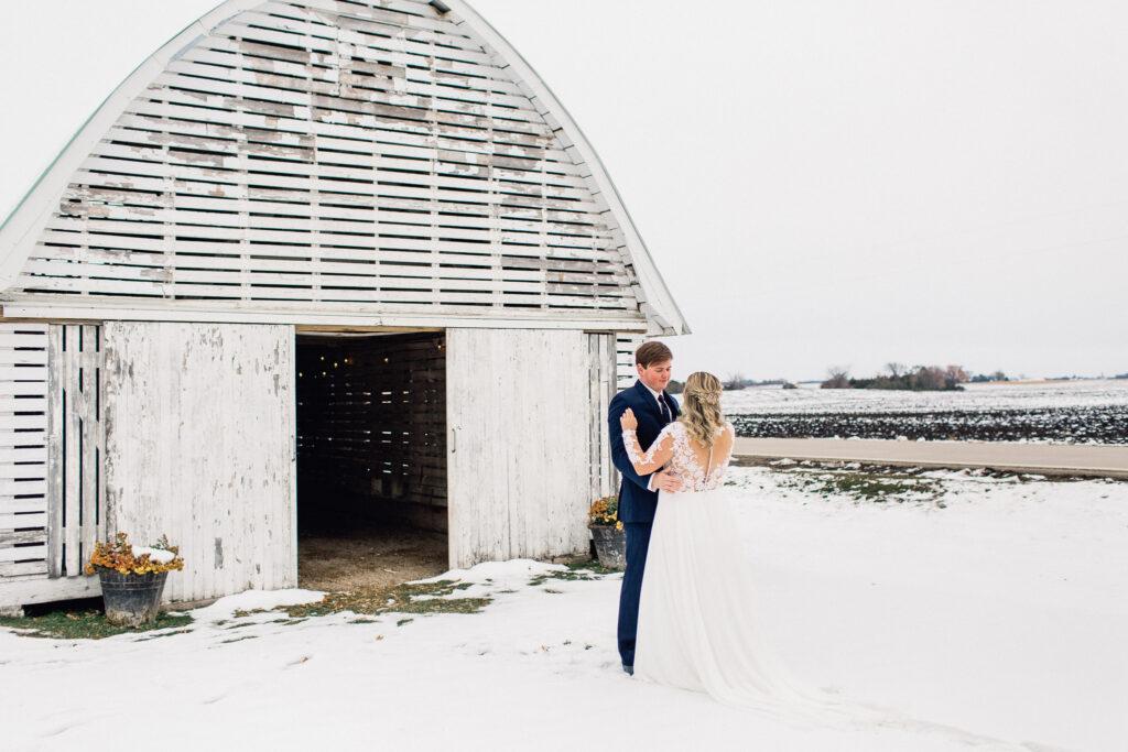 Groom stands with hands on bride's waist, gazing into her eyes during their first look at The Cottage Farmhouse winter wedding.