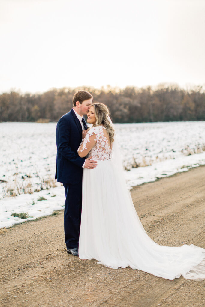 Goom kisses his bride in the head with sunset on the background. She closes her eyes with joy, captured by a Minneapolis wedding photographer at The Cottage Farmhouse.