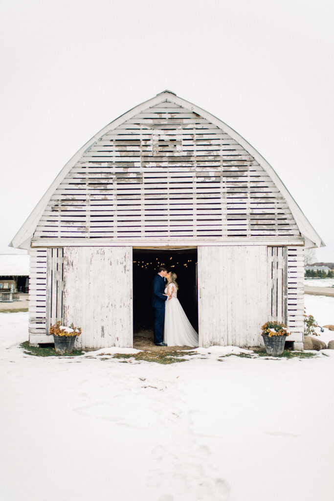 Groom kisses his bride in a small white barn at The Cottage Farmhouse winter wedding.