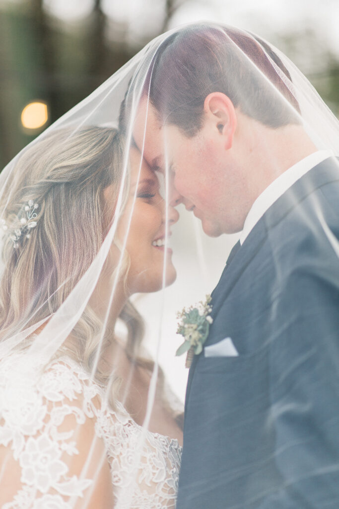 Bride and groom under the vail smiling touching heads.