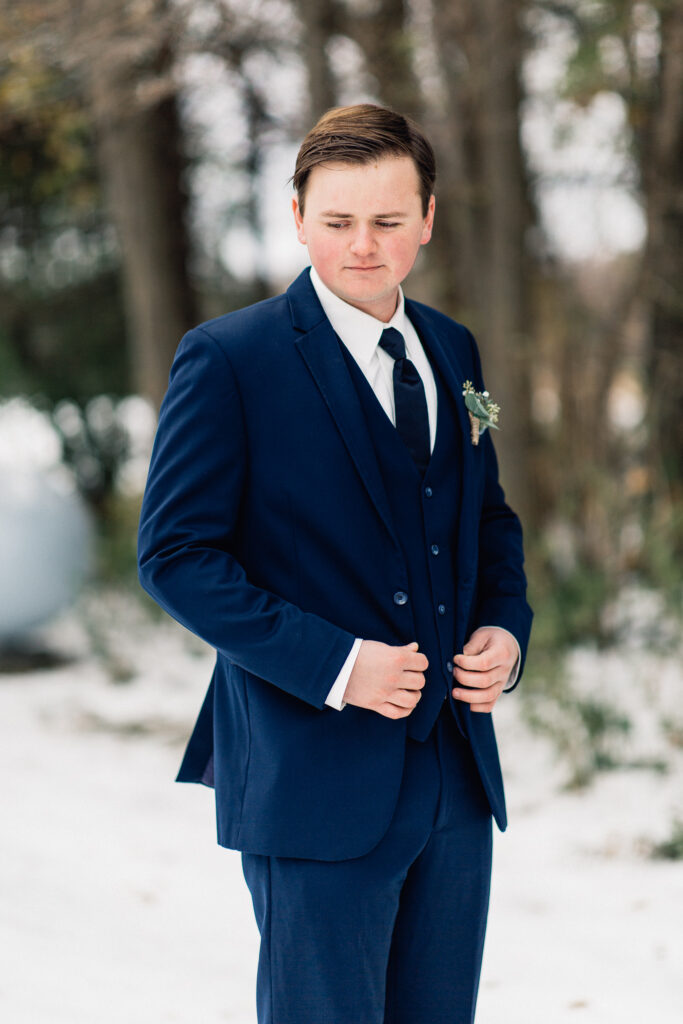 Groom in blue suit looking to the side with hands adjusting his jacket.