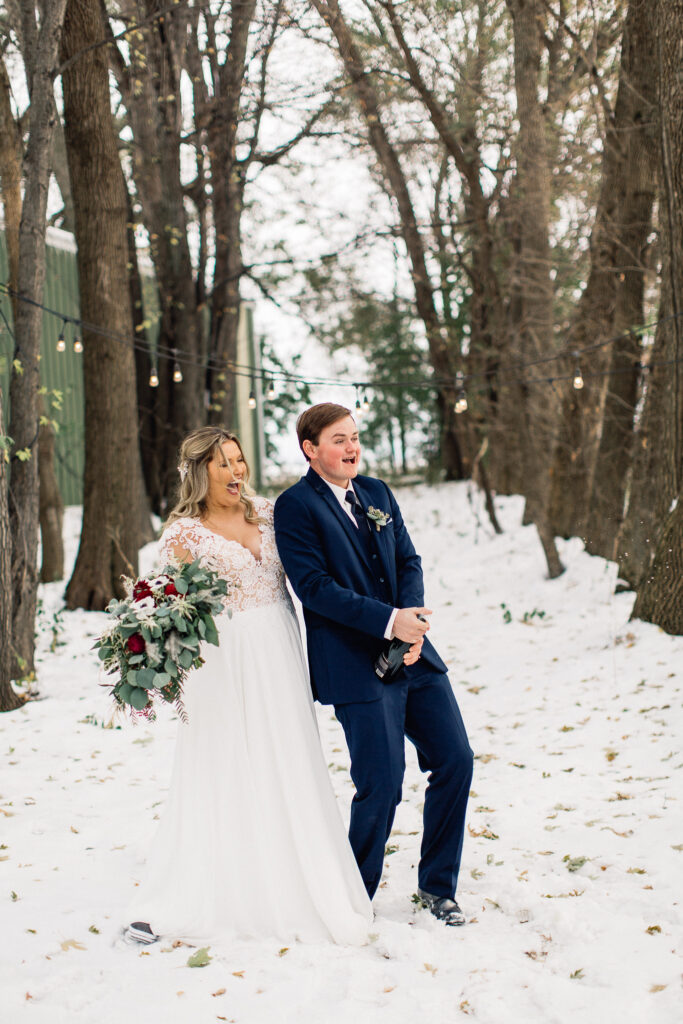 Bride and groom pop champagne bottle with excitement and joy on a wintry day.