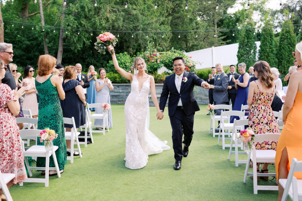 Joyful newlyweds exiting their ceremony at The Hutton House in Minneapolis as guests celebrate and she raises her bouquet, photographed by Minnesota wedding photographer Toly Dzyuba Photography