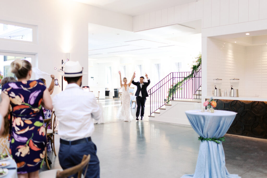 Bride and groom joyfully entering their wedding reception holding hands as guests cheer, captured by Minnesota wedding photographer Toly Dzyuba Photography