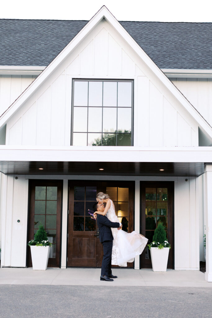 Groom lifting the bride as she kisses his head and laughs at the main entrance of The Hutton House in Minneapolis, captured by Minnesota wedding photographer Toly Dzyuba Photography