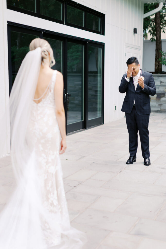 Groom wipes away tears during an emotional first look as he sees his bride for the first time at The Hutton House in Minneapolis, captured by Minnesota wedding photographer Toly Dzyuba.