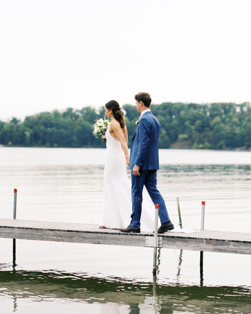Romantic walk on the dock at Madden's on Gull Lake as bride and groom hold hands, captured by Minnesota wedding photographer.