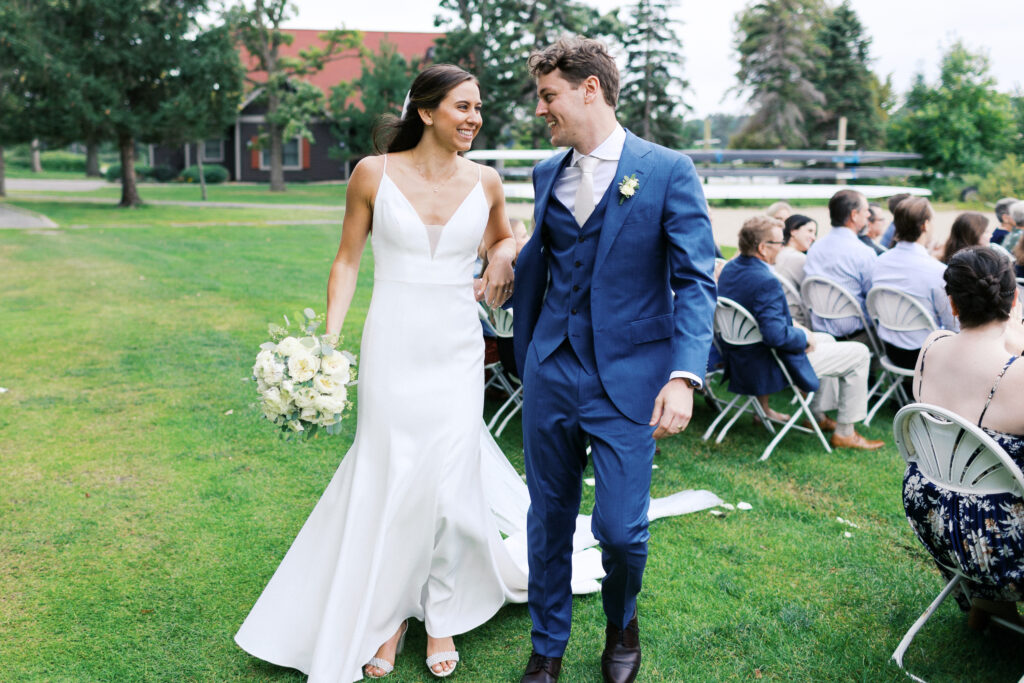 Newly married husband and wife exit the ceremony with joyful smiles, looking at each other as guests cheer.