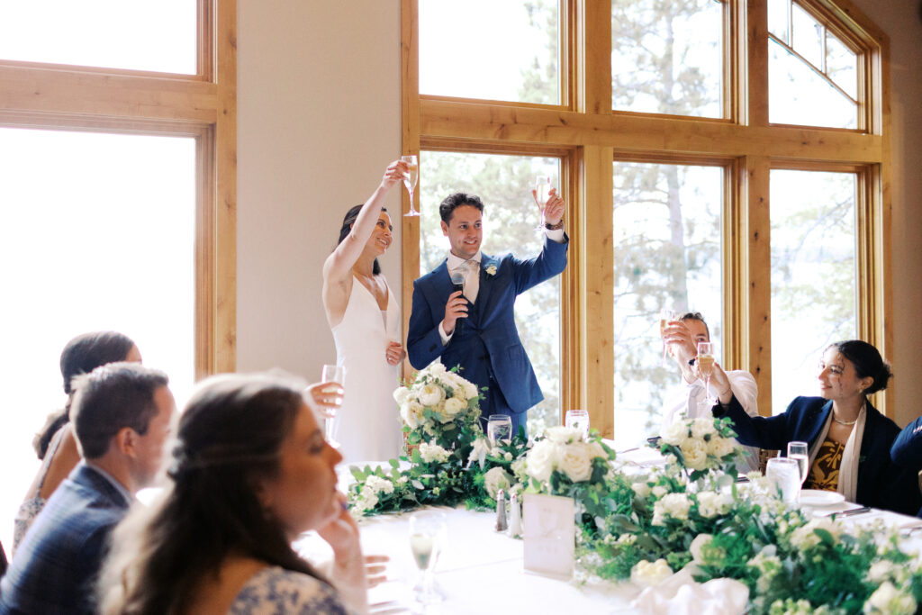 Newlywed couple raising glasses to give toasts during their wedding dinner at Madden’s Resort on Gull Lake, captured by Minnesota wedding photographer.